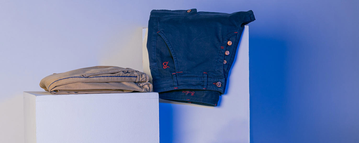 Zwei Hosen liegen auf einem weißen Stufenpodest und werden von einem blauen Licht angeleuchtet.