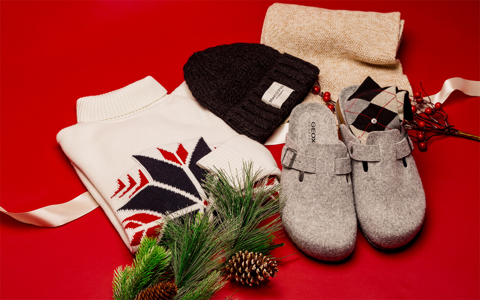 Gemütliches Männer-Geschenkset mit Norwegerpullover, Strickmütze, Wollsocken und grauen Hausschuhen im Winter-Look.