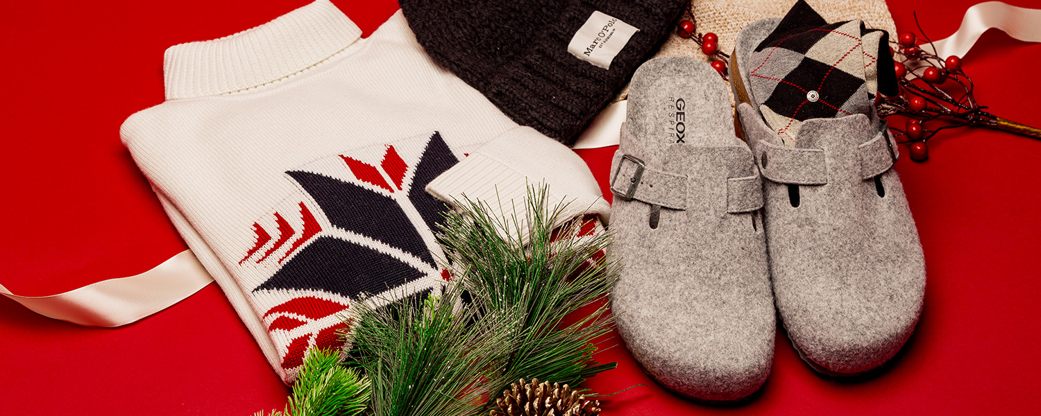 Gemütliches Männer-Geschenkset mit Norwegerpullover, Strickmütze, Wollsocken und grauen Hausschuhen im Winter-Look.