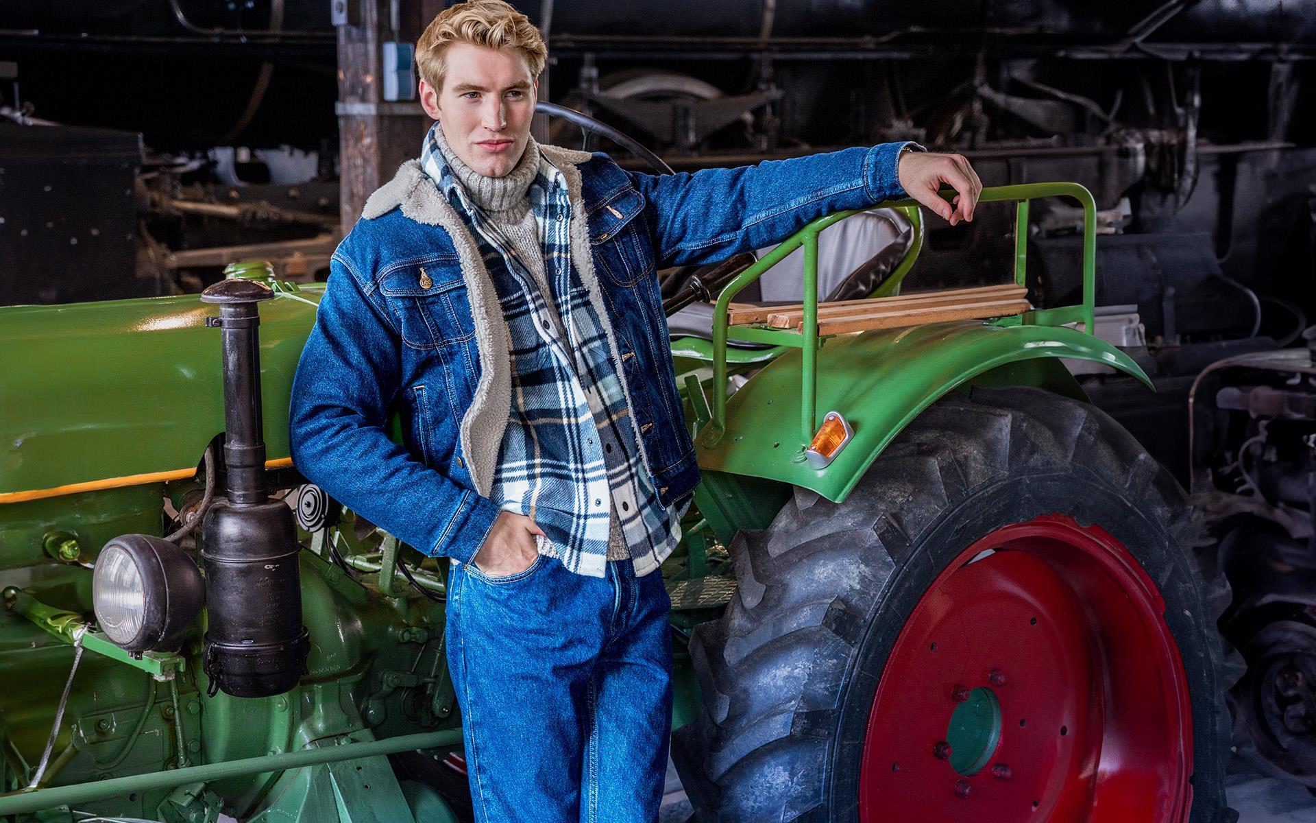 Ein Mann in einer Jeansjacke mit Lammfellfutter, kariertem Overshirt, grauem Rollkragenpullover und blauer Jeans