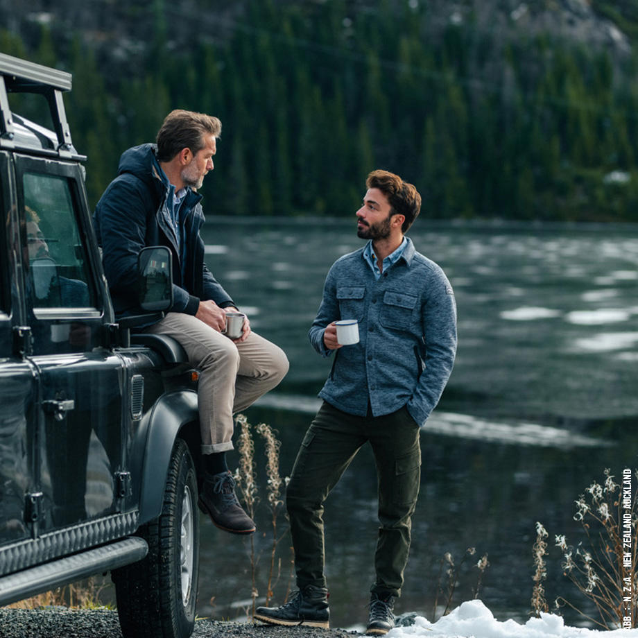 zwei Männer unterhalten sich neben einem Geländewagen mit einer Tasse Kaffee am See