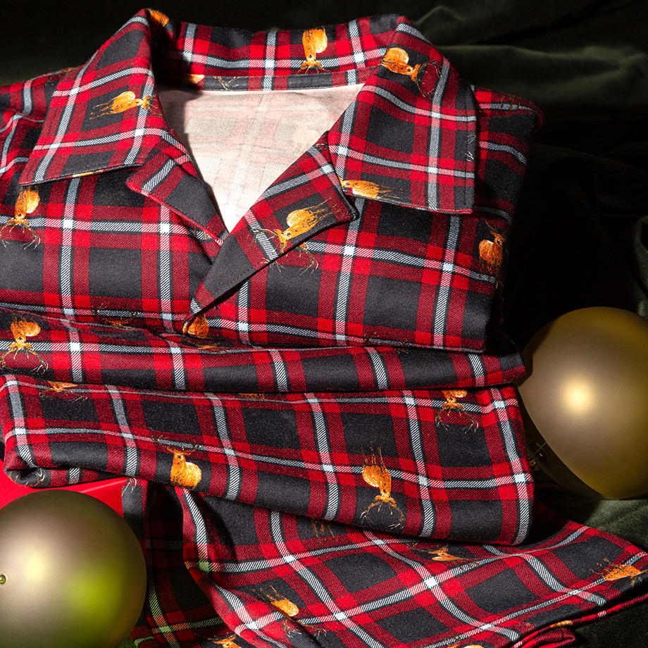 Ein dunkelblau-rot karierter Pyjama mit Hirschmotiven, kombiniert mit einem grünen Hintergrund und festlichen Weihnachtskugeln, verleiht dies eine warme, gemütliche Atmosphäre.