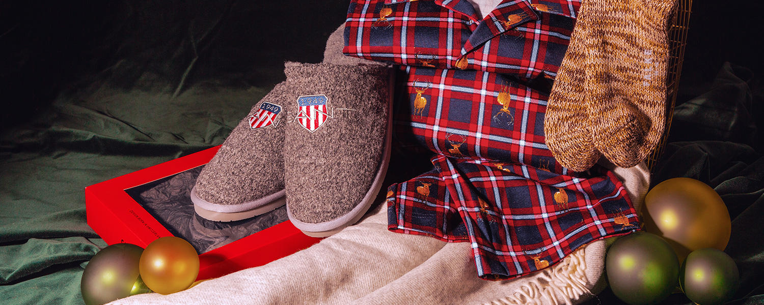 Es sind zu sehen: ein Pyjama, kuschelige Socken, Pantoffeln und ein Schal, umgeben von Weihnachtskugeln