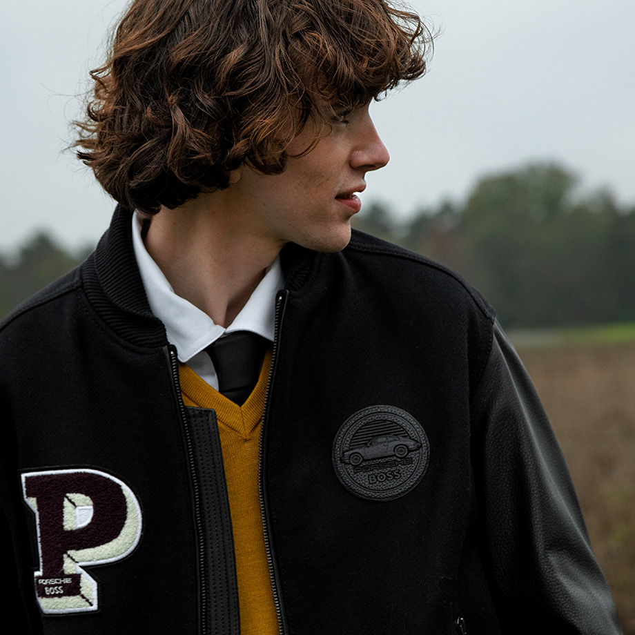 ein junger Mann in College-Jacke, senfgelbem Pullover, weißem Hemd und Krawatte