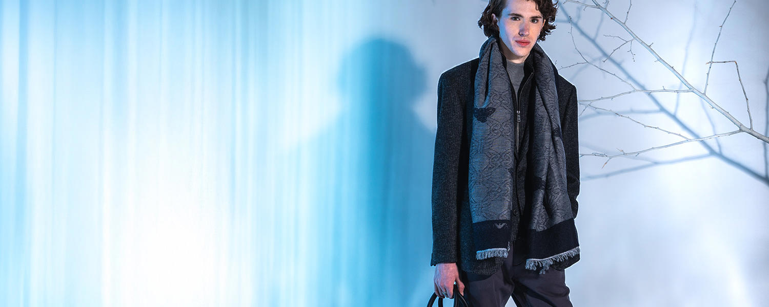 Ein junger Mann in einem grauen, eleganten Layering-Look vor einem Hintergrund mit Eiseffekt und weißen Ästen