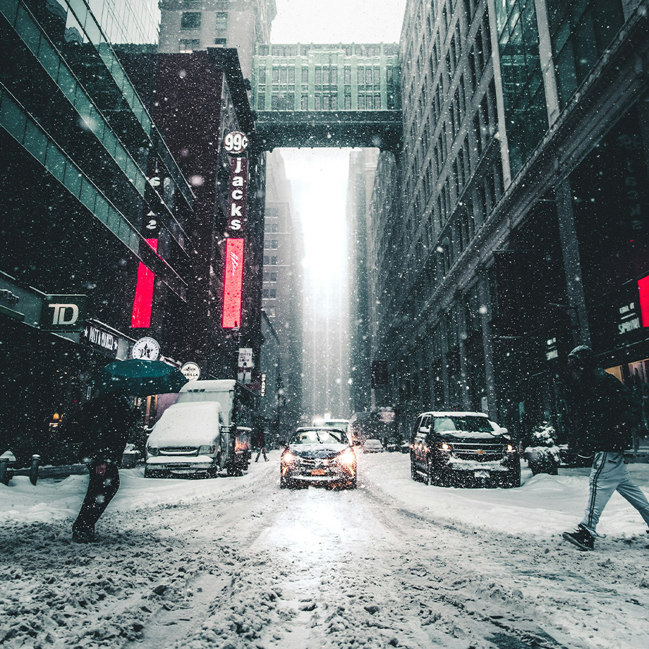 Verschneite Großstadt, die von einer Straße mit Autos und Fußgängern fotografiert wurde..