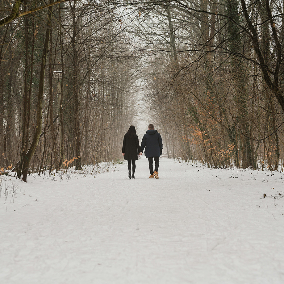 Ein Pärchen geht durch einen verschneiten Wald spazieren.