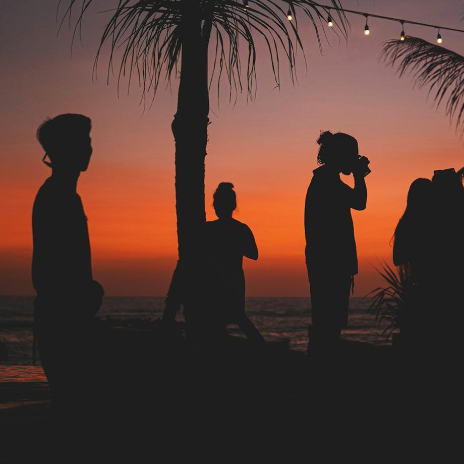 Silhouetten einiger Menschen vor dem Sonnenuntergang, Lichterketten und Palmen