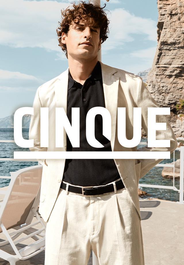 Ein Mann mit beigem Anzug vor sommerlicher Strandkulisse repräsentiert die CINQUE Sommer Kollektion 