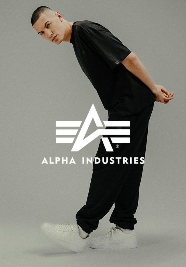 Alt Text: Ein Mann trägt ein schwarzes T-Shirt und  schwarze Hose von Alpha Industries