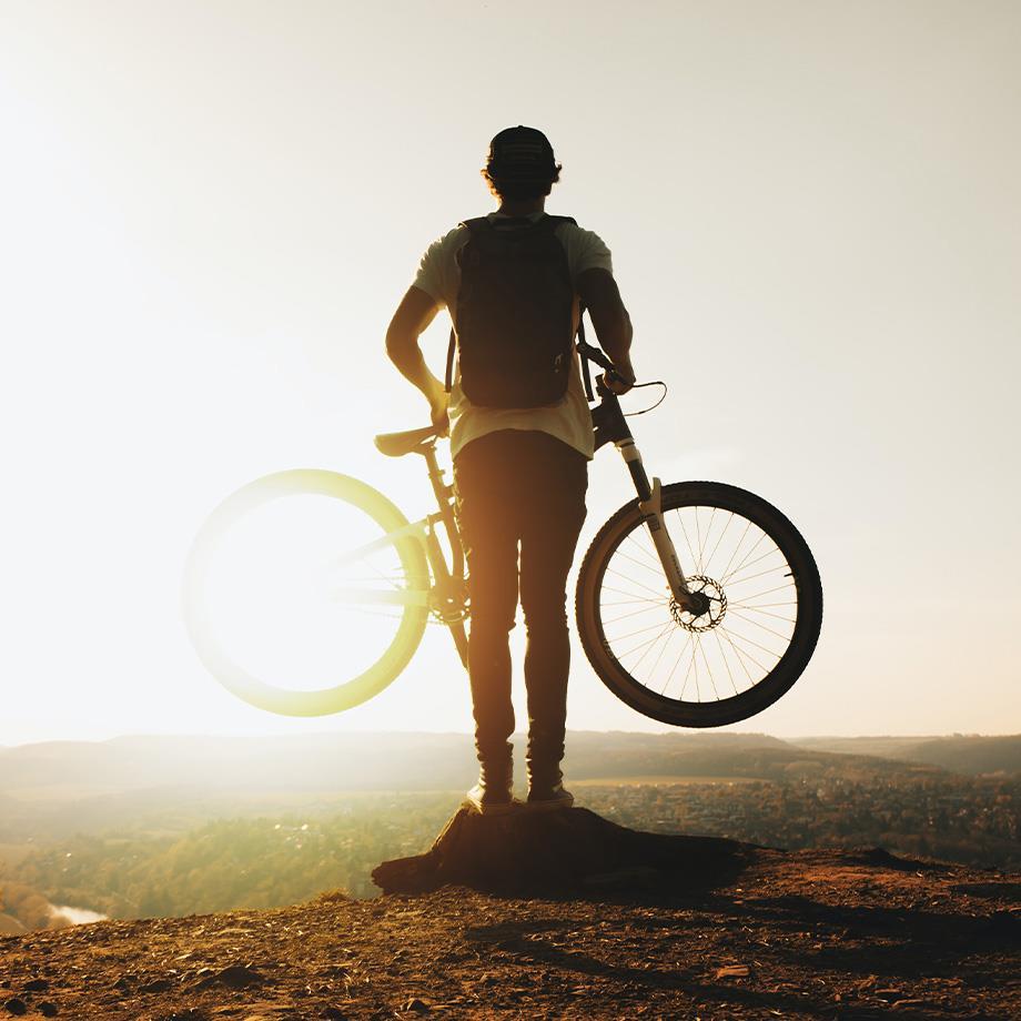 Ein Mann in weißem T-Shirt und langer Hose mit Fahrrad bei Sonnenuntergang