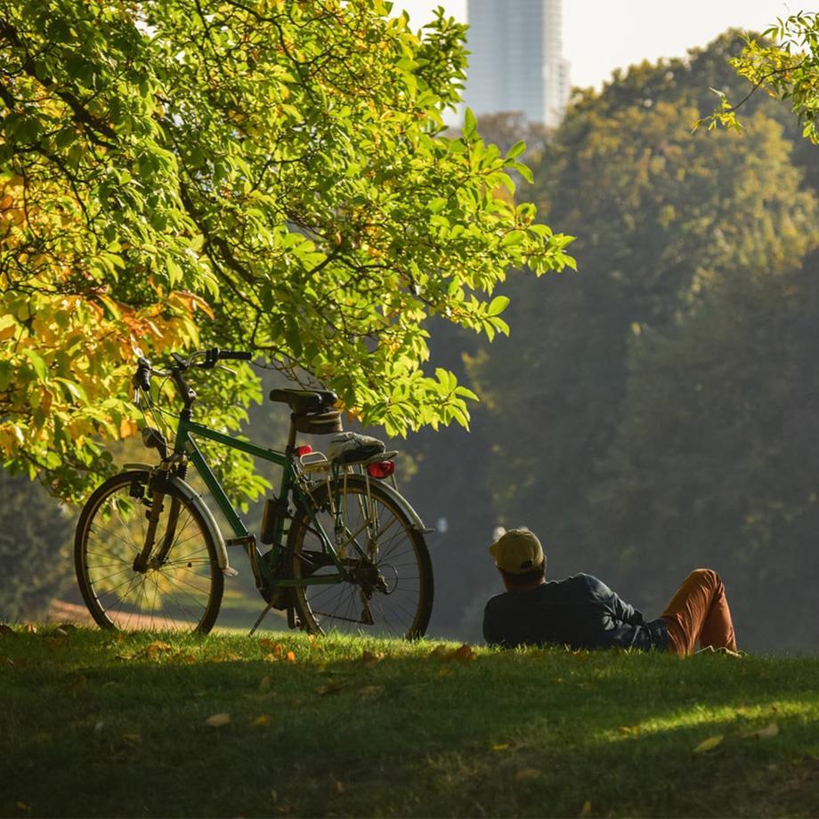 Ein Mann liegt im Park auf der Wiese, daneben steht sein Fahrrad.