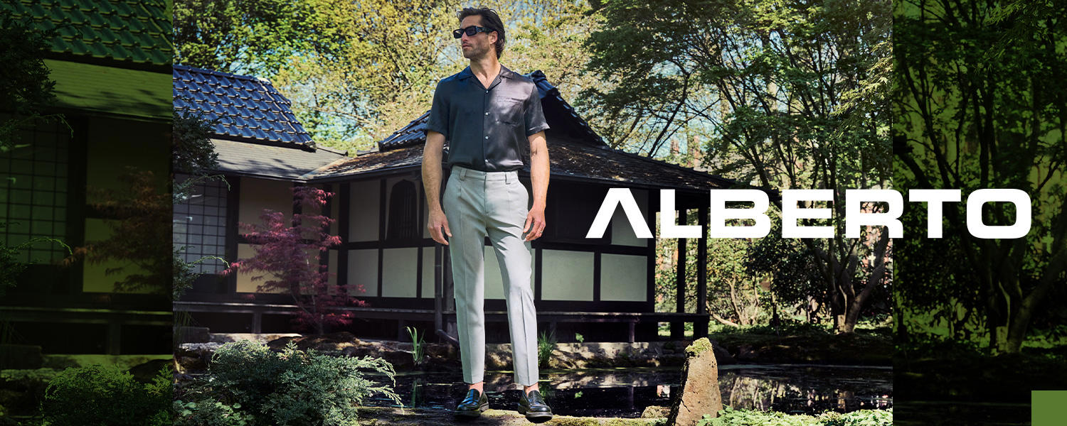 Mann steht in einer ALBERTO-Hose auf einem Stein. Er trägt ein Kurzarmhemd und eine schwarze Sonnenbrille. 