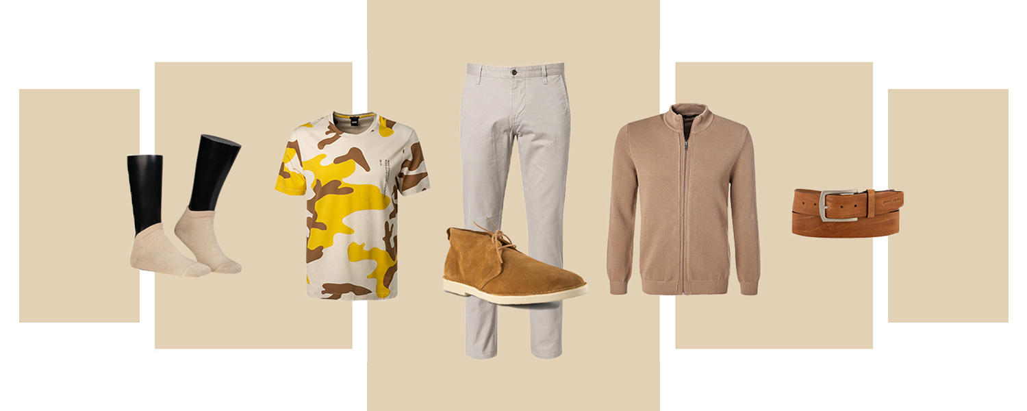Ein Outfit bestehend aus beigen Socken, einem T-Shirt in Tarnfarben, einer beigen Chino, Desert Boots, einer Strickjacke in Beige und einem braunen Gürtel.