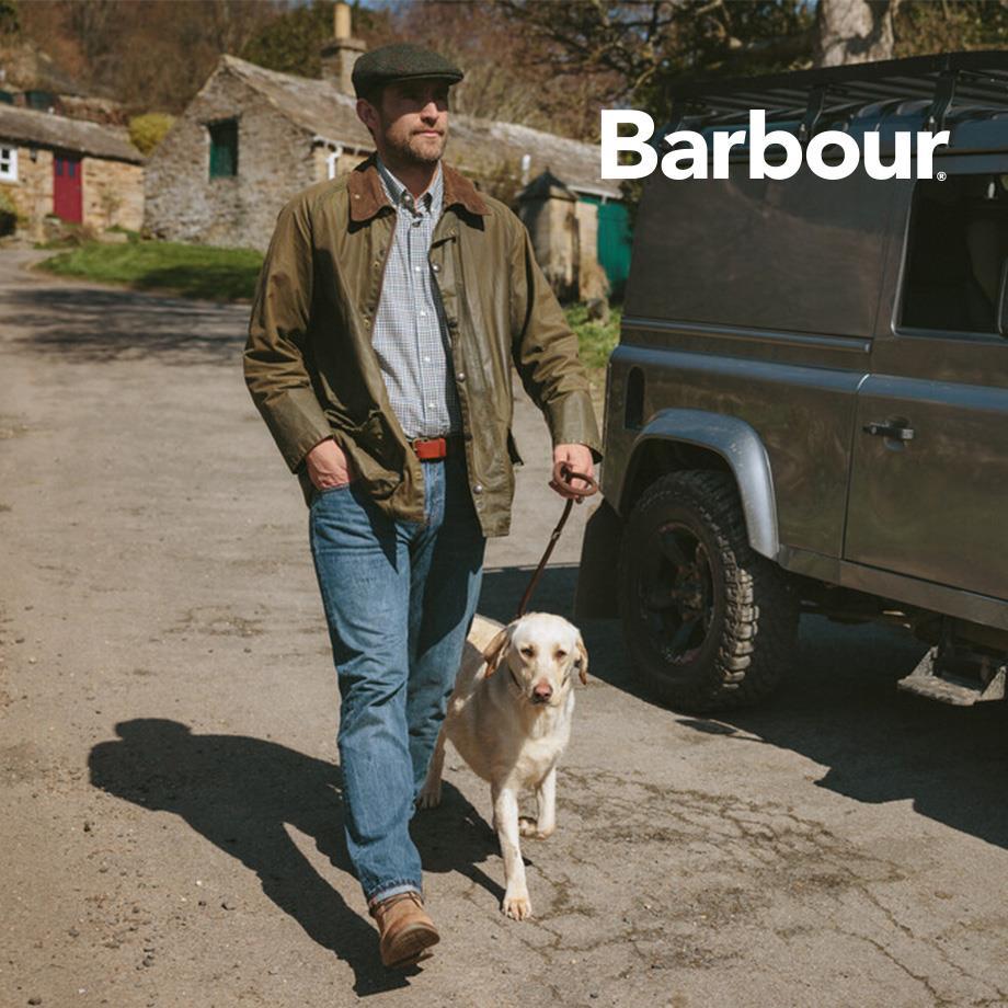 Ein Mann trägt eine grüne Barbour Wachsjacke mit Cordkragen, kombiniert mit einem karierten Hemd und Jeans.