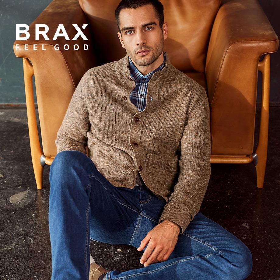 Ein Mann trägt blaue Jeans von Brax und passend dazu einen beigen Cardigan.