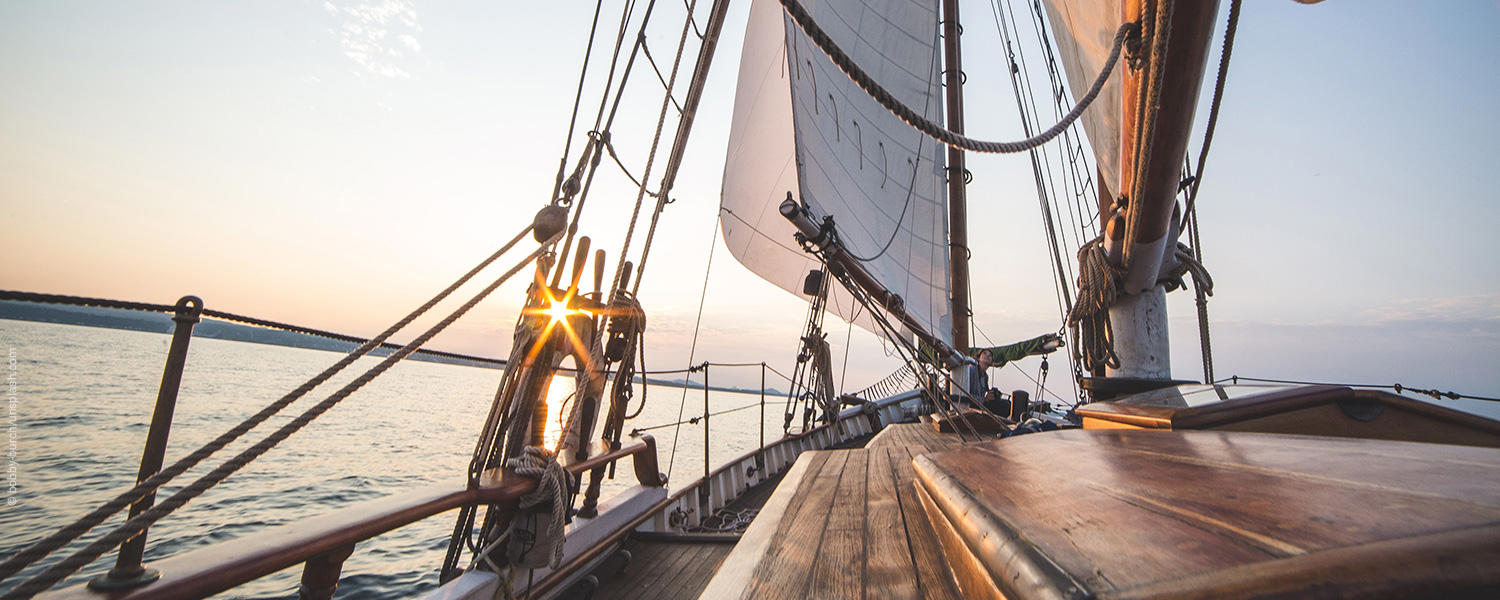 Ein Segelschiff segelt dem Sonnenuntergang entgegen. 