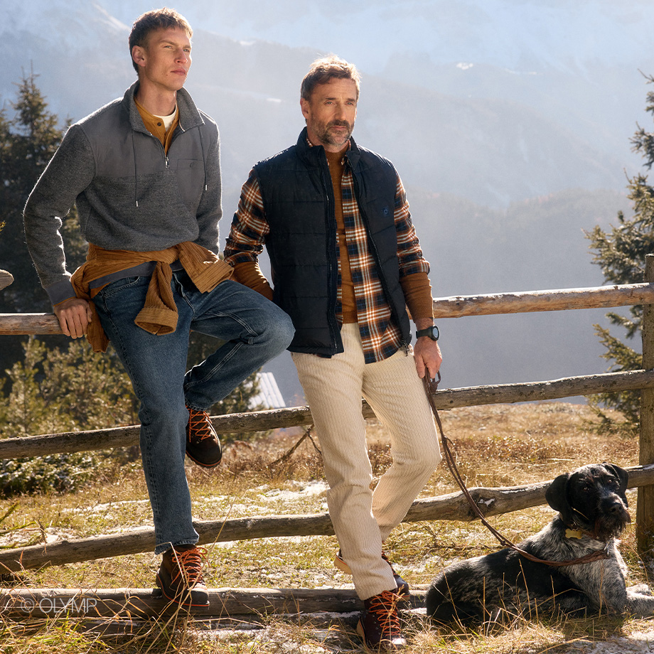 OLYMP Herrenmode Herbst/Winter – zwei Männer in Freizeit-Looks mit Pullover, Karo-Hemd und Weste in den Bergen. 