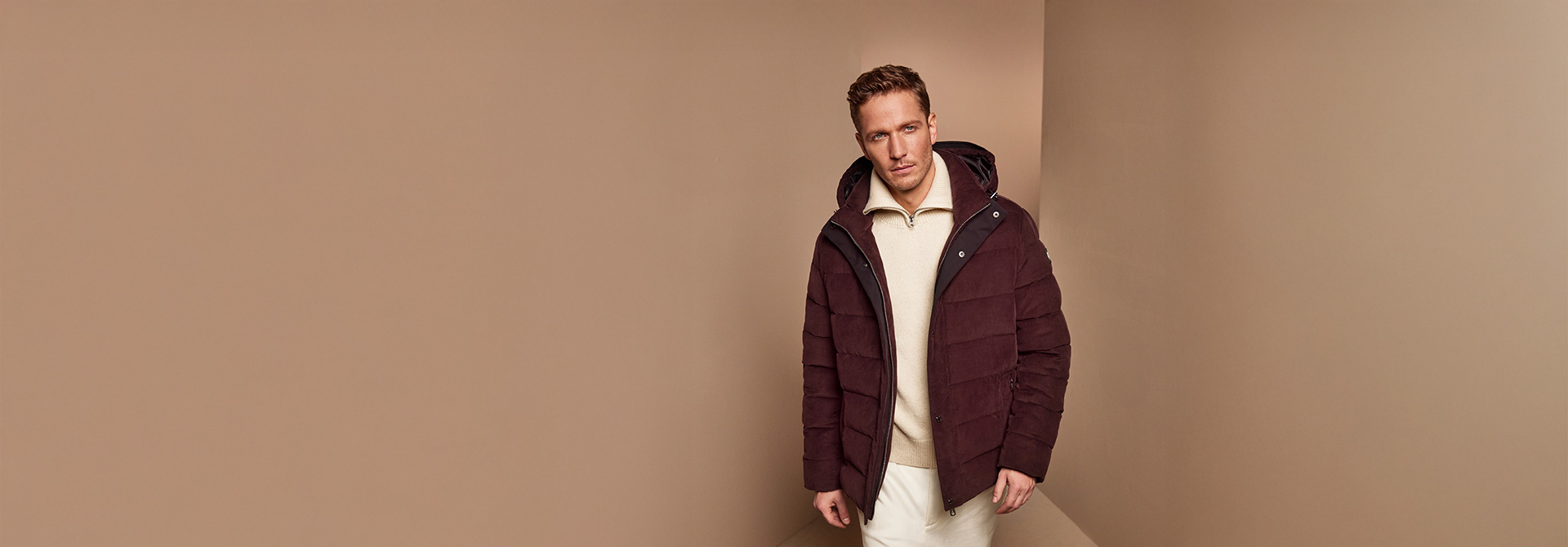 Mann in burgunderfarbener Steppjacke aus Polyester, hellem Pullover, elegant präsentiert