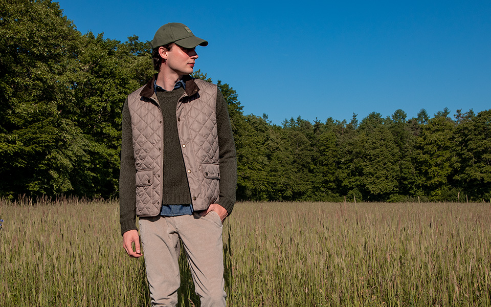 Ein junger Mann trägt eine beige Steppweste im stilvollen Layering