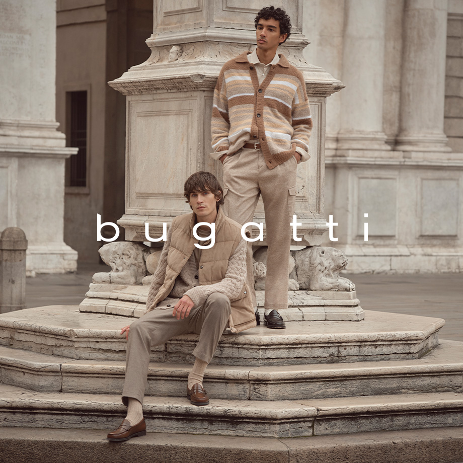 Herren in beiger Strickjacke und Weste, kombiniert mit Anzughose an historischer Säule