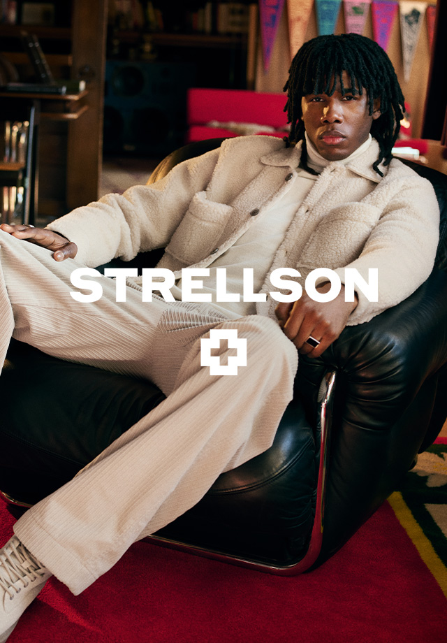 Mann im cremefarbenen Cordanzug auf schwarzem Sessel sitzend, lässiger Look