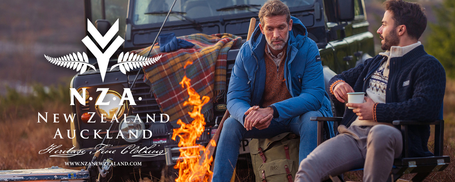 Männer im Gespräch, tragen blaue Daunenjacke und Norweger-Strickjacke, sitzen am Lagerfeuer.