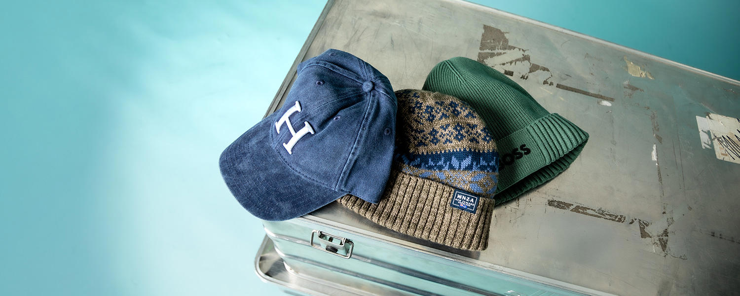 Blaue Cap, grünes Beanie und gemusterte Wollmütze auf Metallkoffer präsentiert