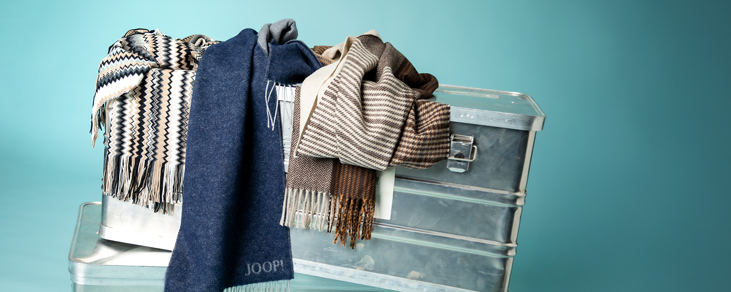 Herren-Wollschals in Blau und Brauntönen, gestreift und gemustert, auf Metallbox drapiert