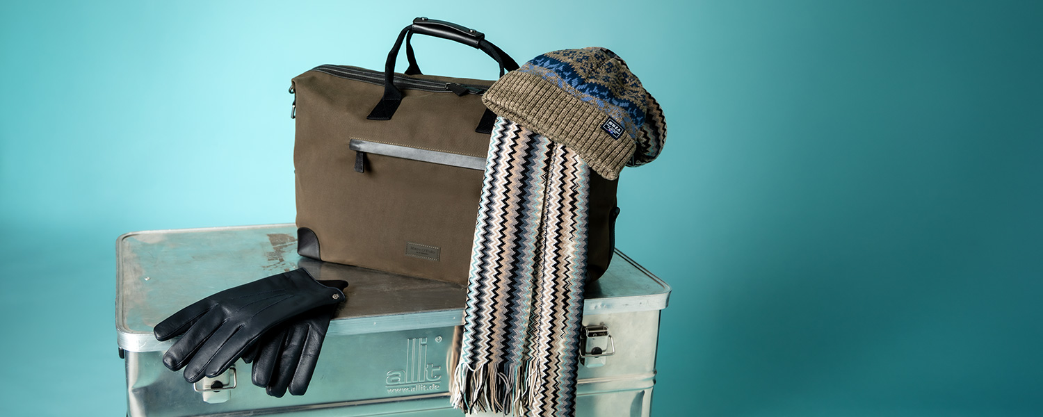 Braune Umhängetasche mit Strickmütze, Schal und schwarzen Lederhandschuhen auf Metallbox