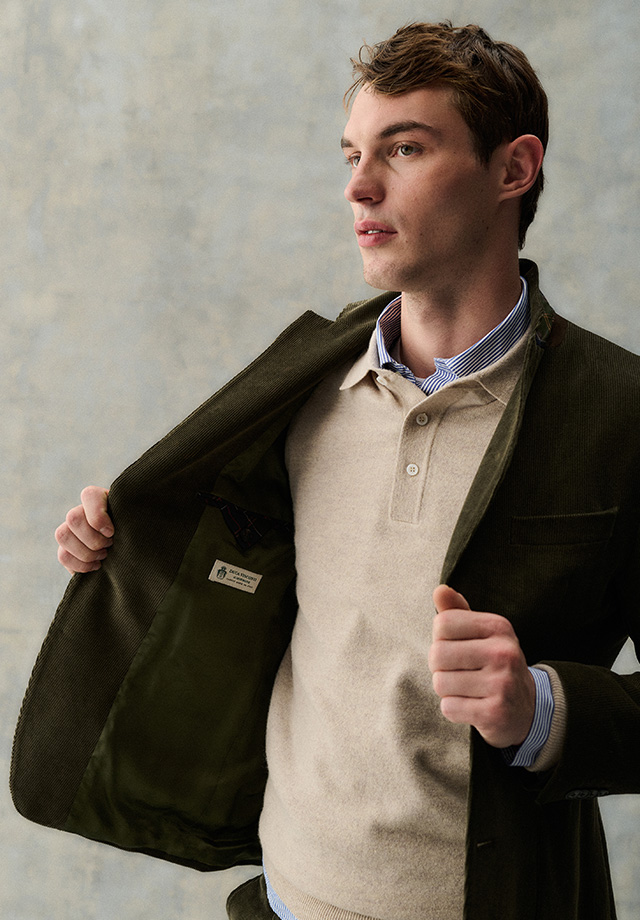 Mann in beigefarbenem Poloshirt und olivgrünem Jackett über gestreiftem Hemd, elegant getragen