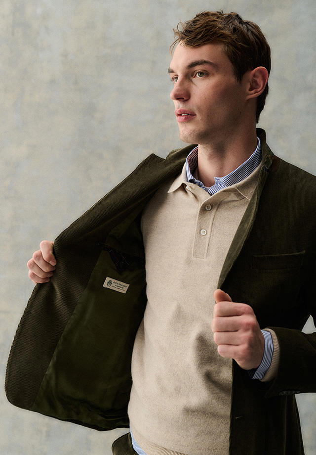 Mann in beigefarbenem Poloshirt und olivgrünem Jackett über gestreiftem Hemd, elegant getragen