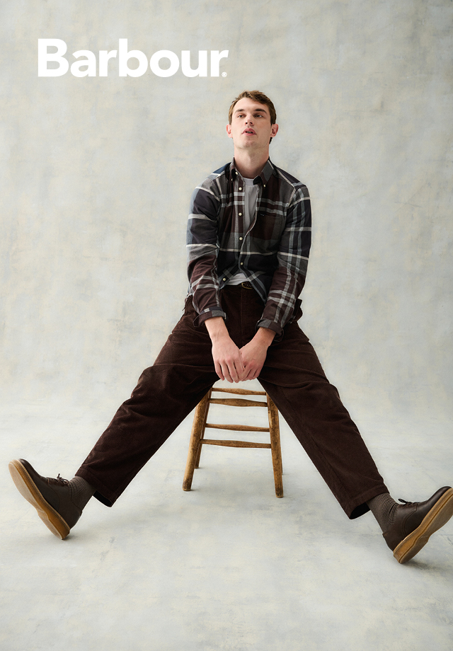 Kariertes Freizeithemd in Grau-Braun, getragen mit brauner Cordhose und Stiefeln auf Stuhl sitzend