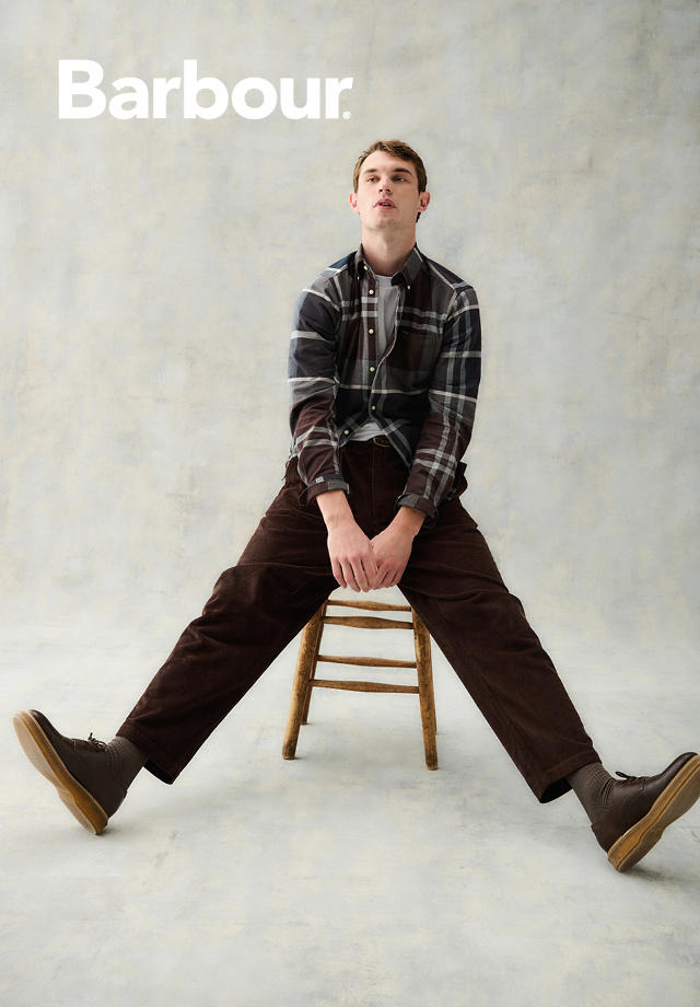 Kariertes Freizeithemd in Grau-Braun, getragen mit brauner Cordhose und Stiefeln auf Stuhl sitzend