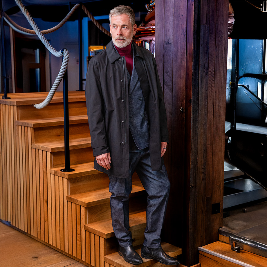 Mann in grauem Wollanzug mit schwarzem Mantel, Business-Look