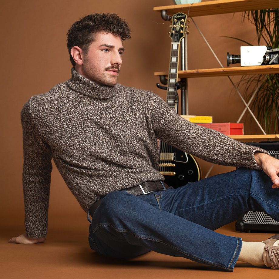 Mann in meliertem Rollkragenpullover aus Strick, lässig sitzend mit blauer Jeans