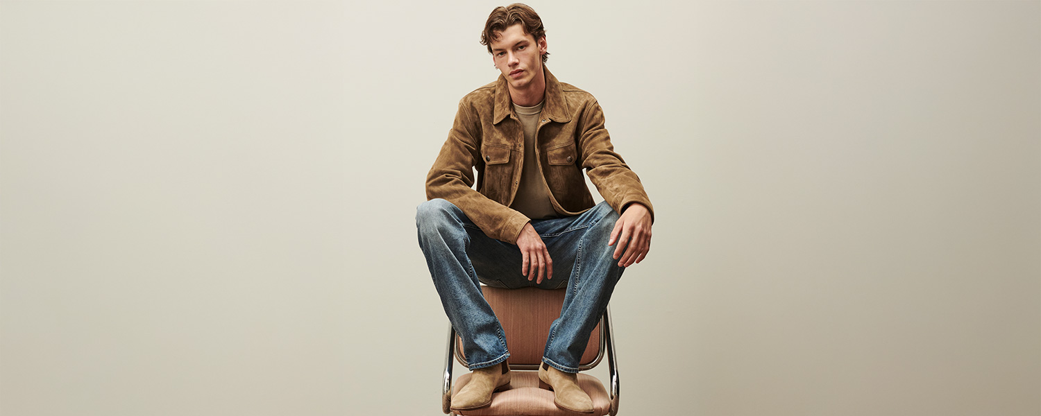 Mann in brauner Wildlederjacke mit Jeans, leger im Stuhl sitzend