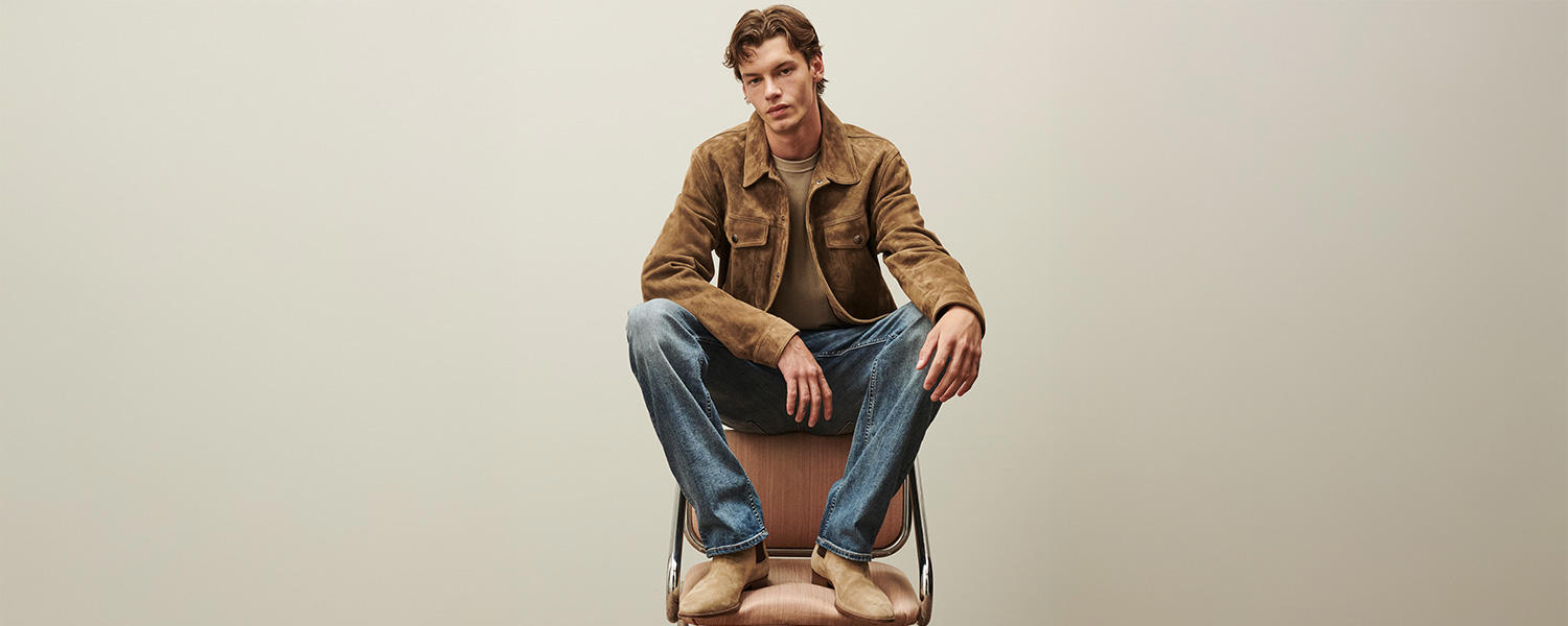 Mann in brauner Wildlederjacke und blauer Jeans, lässig auf Stuhl sitzend