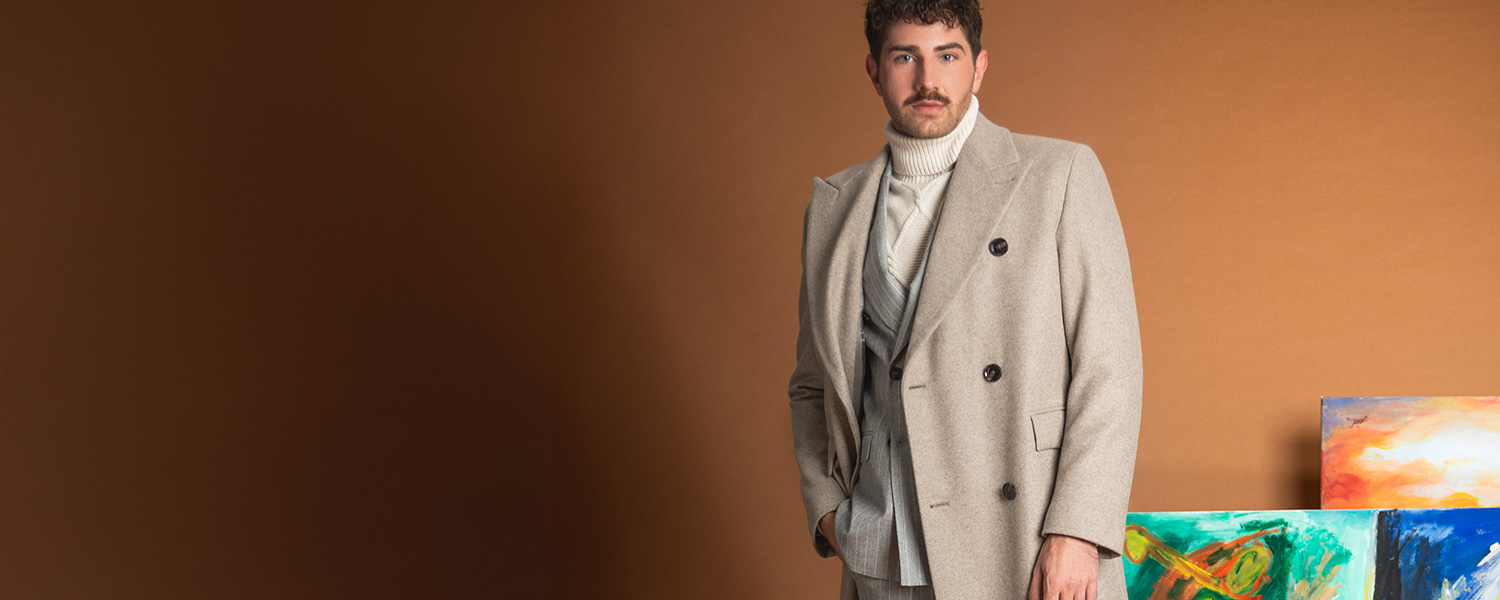 Hellgrauer Wollmantel über cremefarbenem Rollkragenpullover, Mann in Atelier stehend