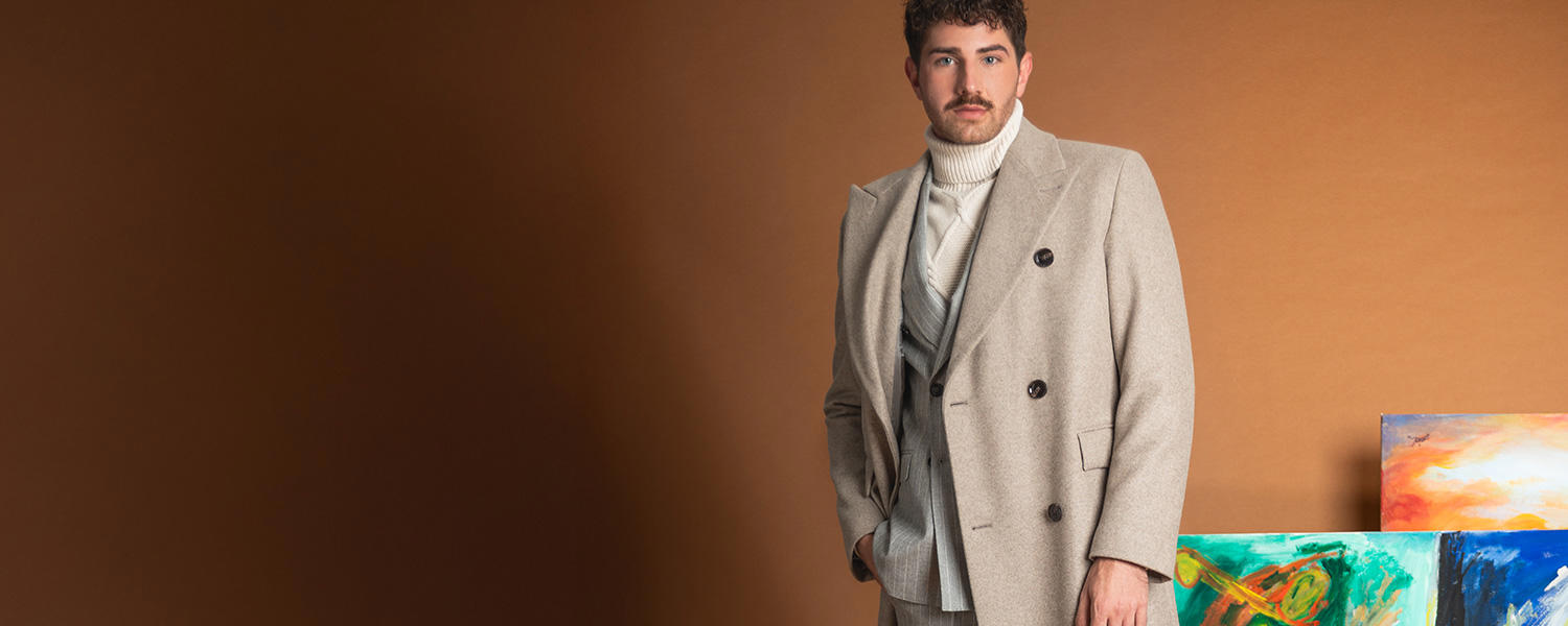 Hellgrauer Wollmantel über cremefarbenem Rollkragenpullover, Mann in Atelier stehend