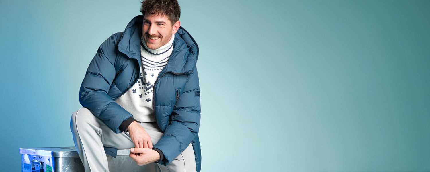Mann in blauer Daunenjacke und weißem Norwegerpullover, sitzend, lässiger Winterlook