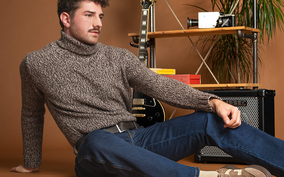 Mann in meliertem Rollkragenpullover aus Strick, lässig sitzend mit blauer Jeans