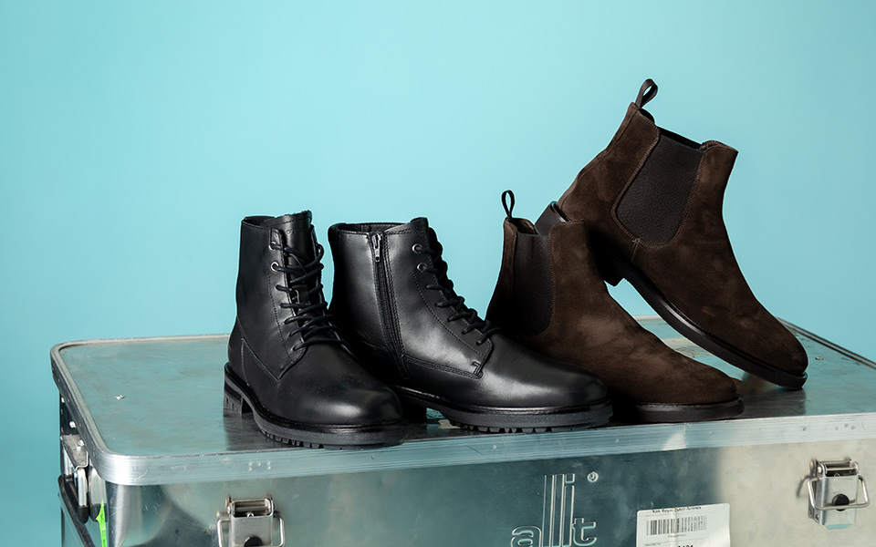 Schwarze Lederstiefel und braune Wildleder-Chelsea-Boots auf Metallkiste, elegant und hochwertig