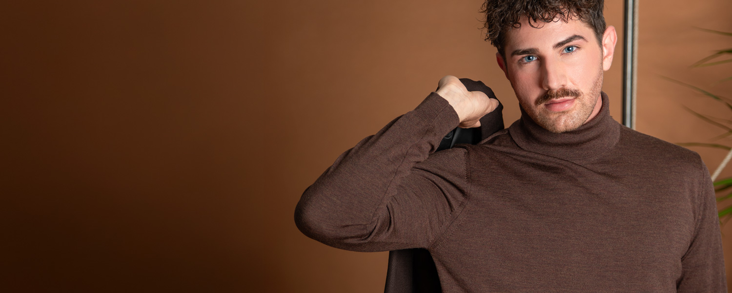 Herr in braunem Rollkragenpullover aus feiner Wolle, lässig Schultersakko tragend.