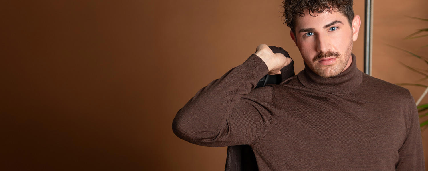 Herr in braunem Rollkragenpullover aus feiner Wolle, lässig Schultersakko tragend.