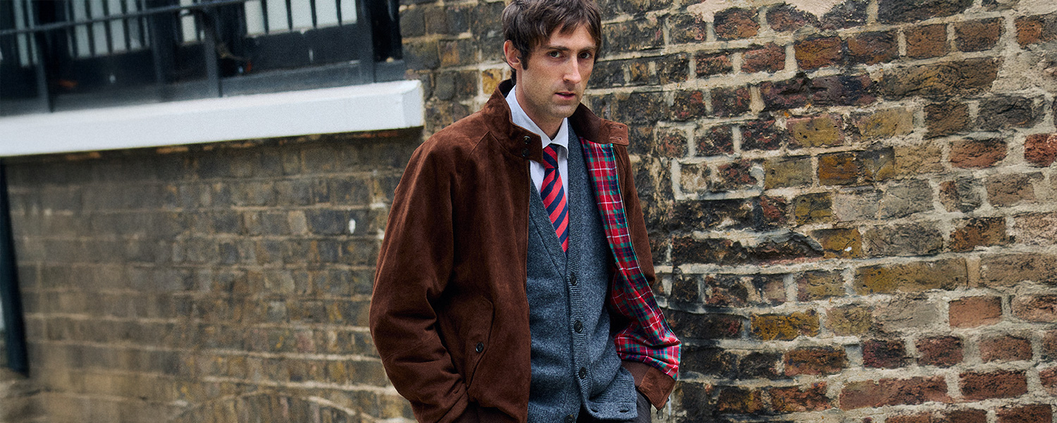 Mann in brauner Wildlederjacke mit Wollweste und gestreifter Krawatte, lässig kombiniert