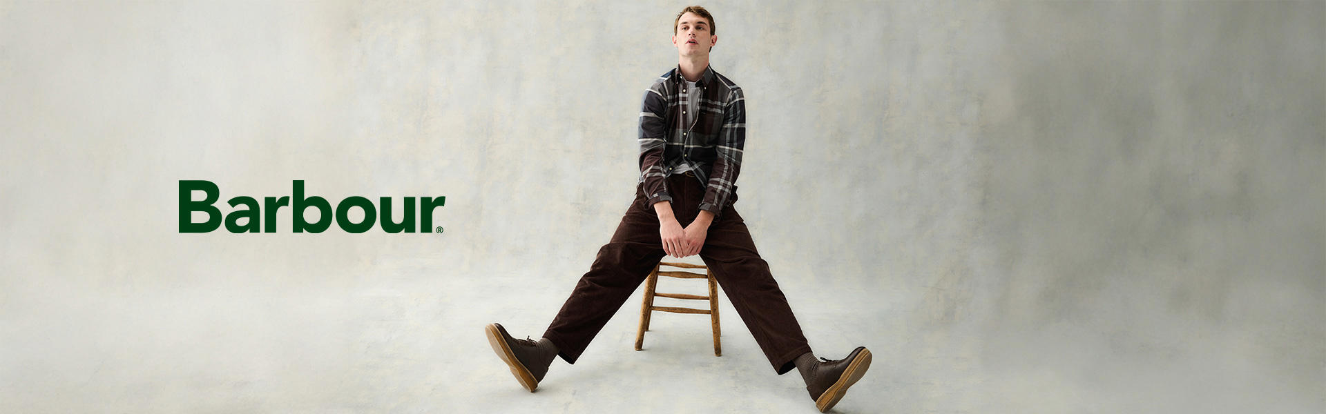 Kariertes Freizeithemd in Grau-Braun, getragen mit brauner Cordhose und Stiefeln auf Stuhl sitzend