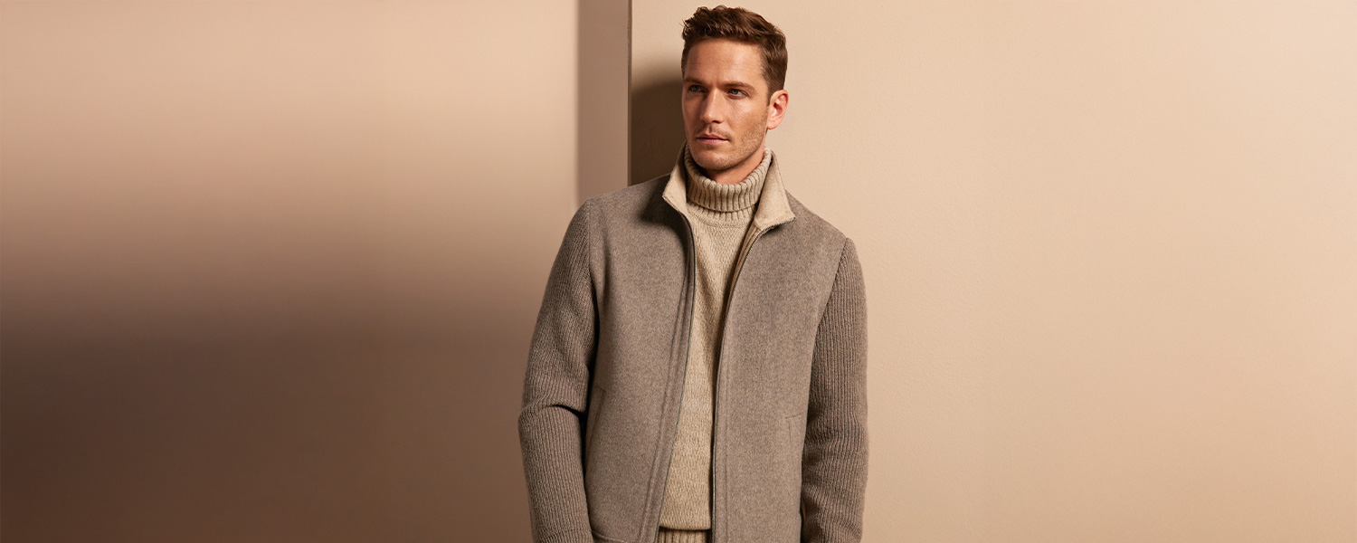 Mann in grauem Wollmantel und beigem Rollkragenpullover, elegant vor neutralem Hintergrund