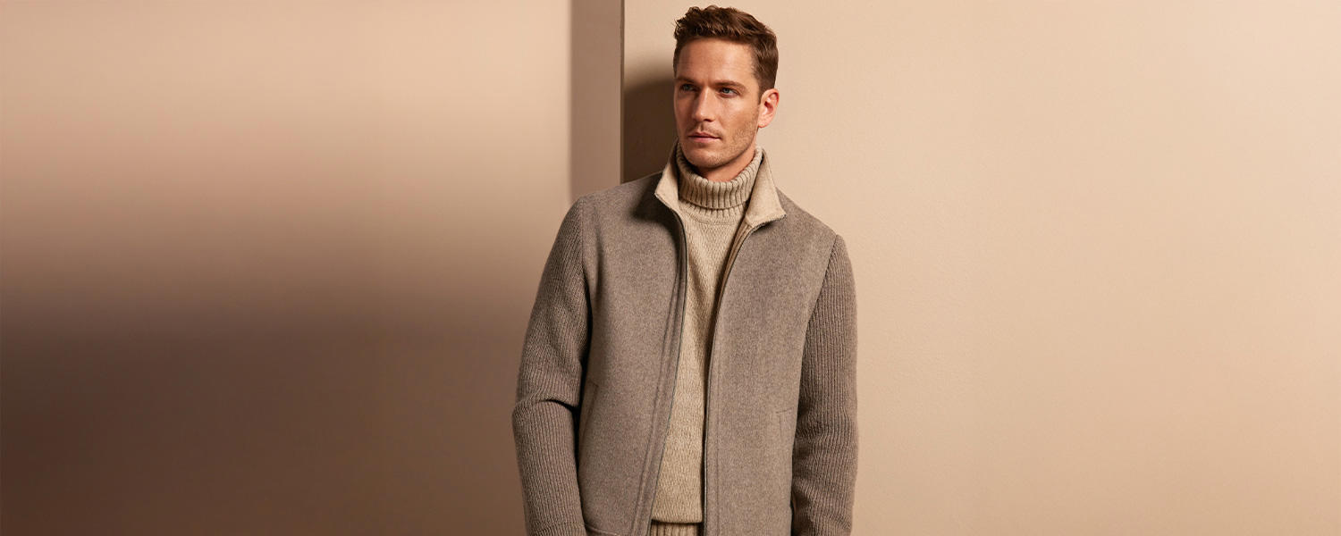 Mann in grauem Wollmantel und beigem Rollkragenpullover, elegant vor neutralem Hintergrund