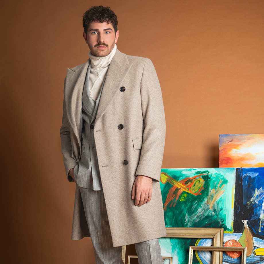 Eleganter grauer Wollmantel über Streifenanzug, getragen von Mann im Atelier